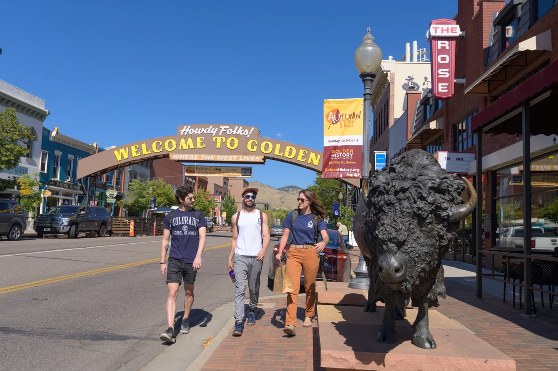 Three students walk downtown Golden and pass by a statue of a buffalo.