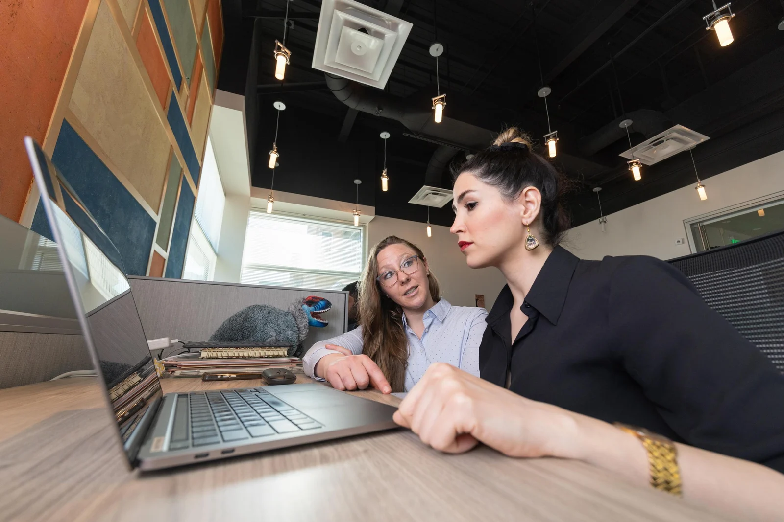 A student and professor collaborate at a desk with a laptop in a modern office.