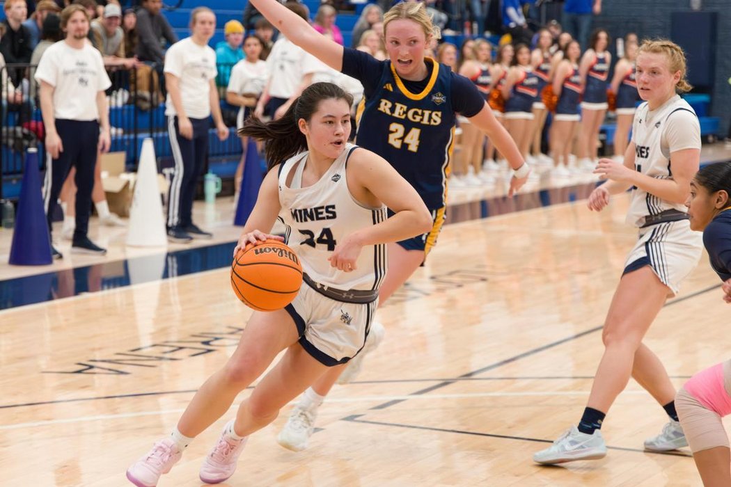 Mines women's basketball athlete dribbling the ball on court through the opposing team's defense.