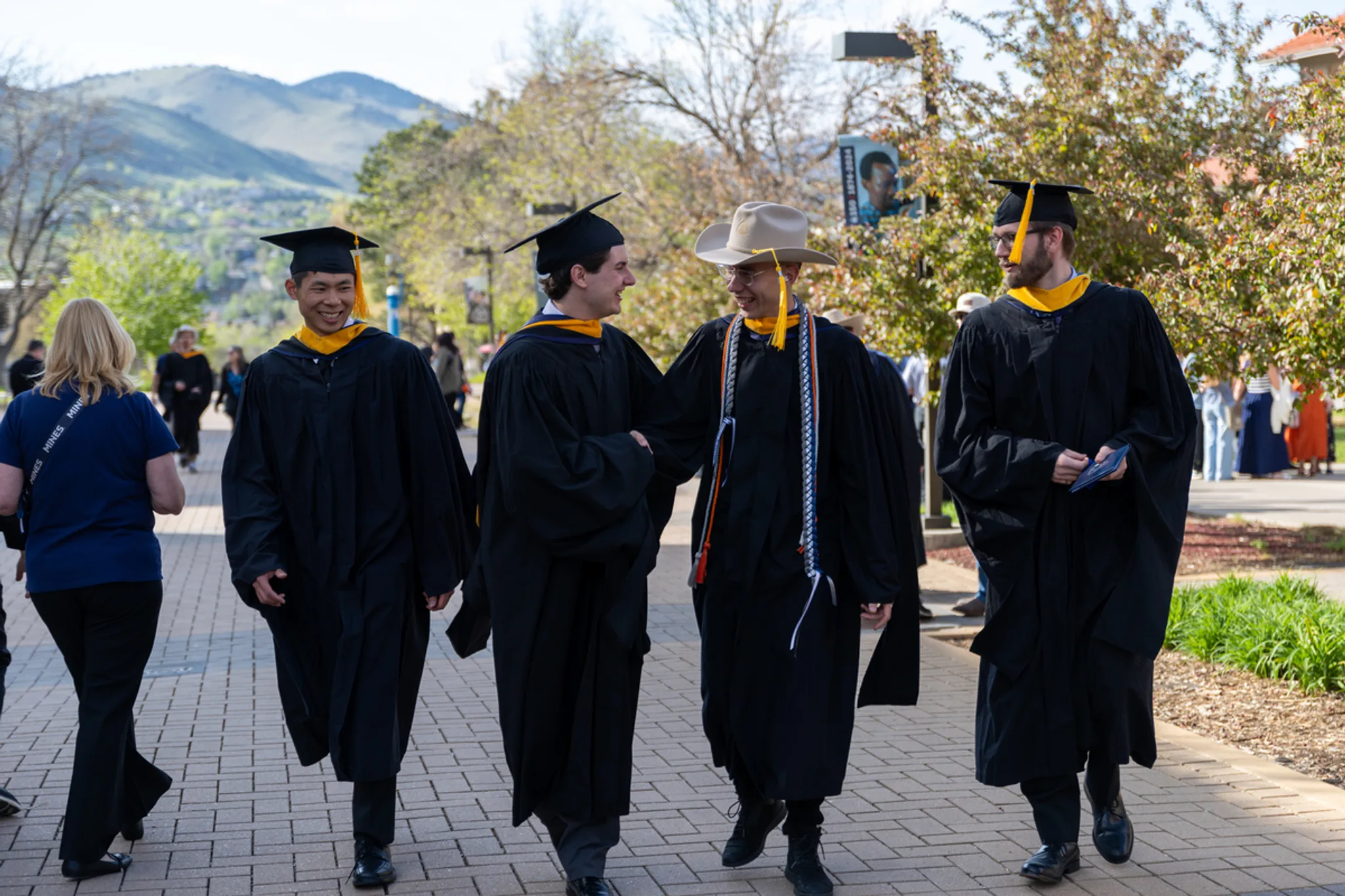 Mines recent graduates walking outside wearing Mines hat and gown