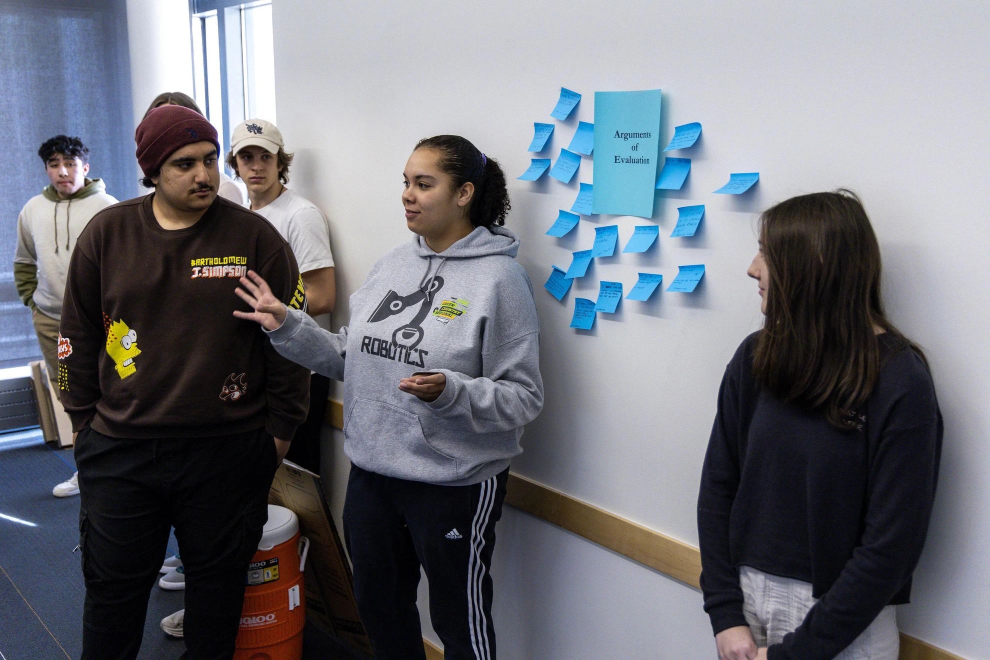 Several students engage in a brainstorming session, gathered around a wall filled with various sticky notes in different colors.