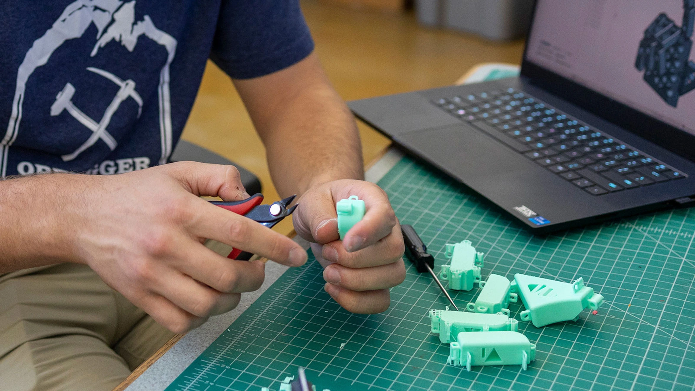 A man sitting at a table with a laptop and a pair of pliers.