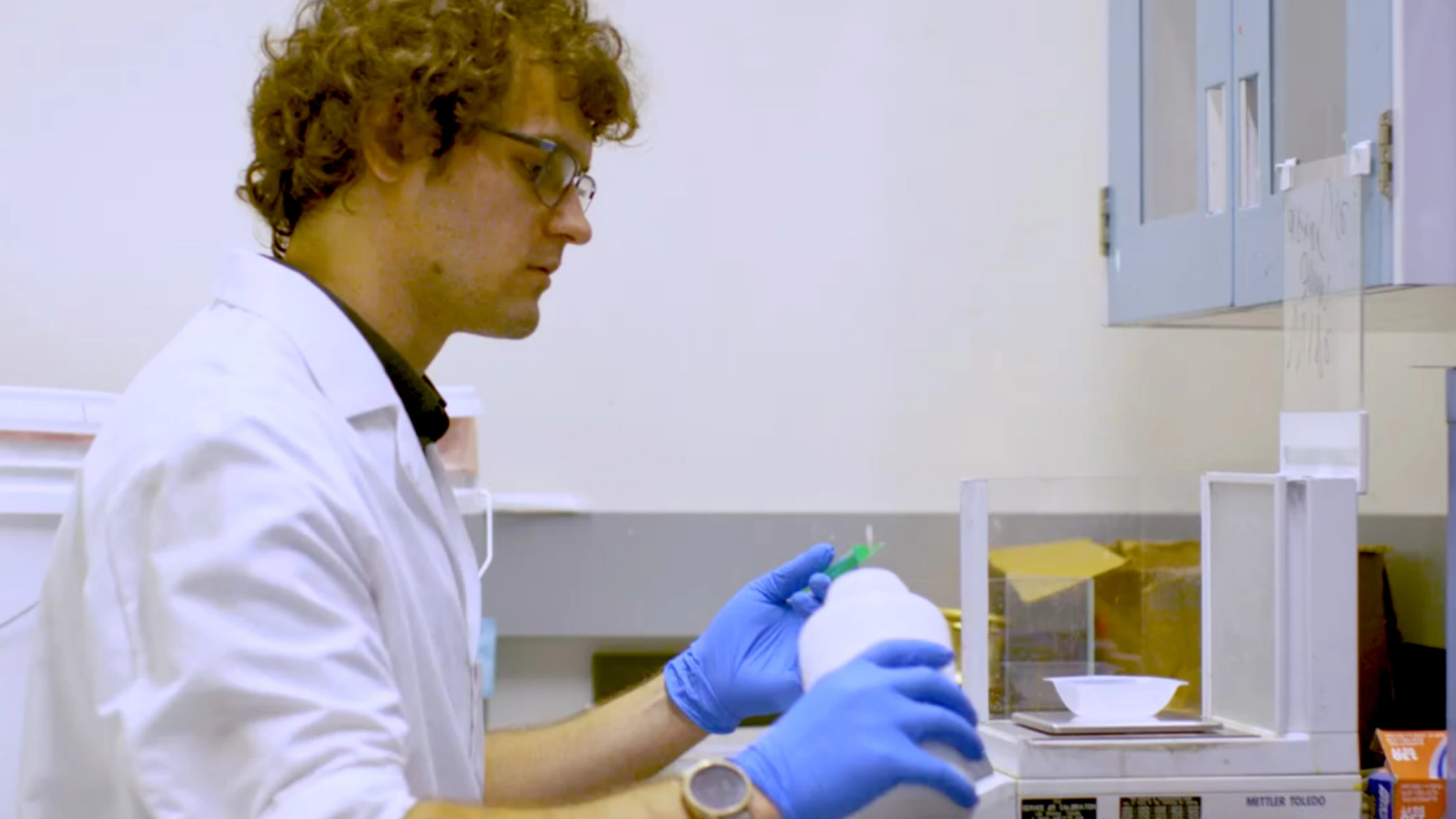 A man in a lab coat and blue gloves working in a laboratory.