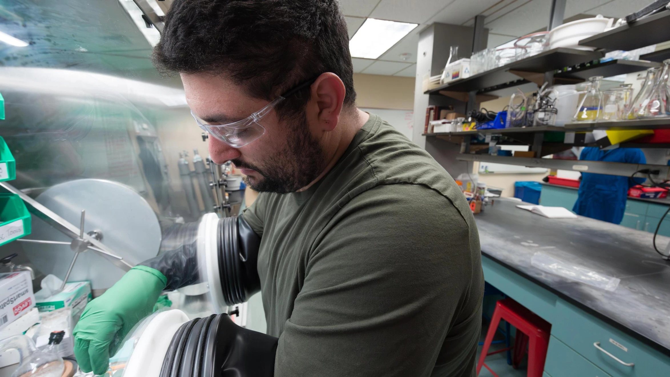 A man in a green shirt and green gloves working in a laboratory.