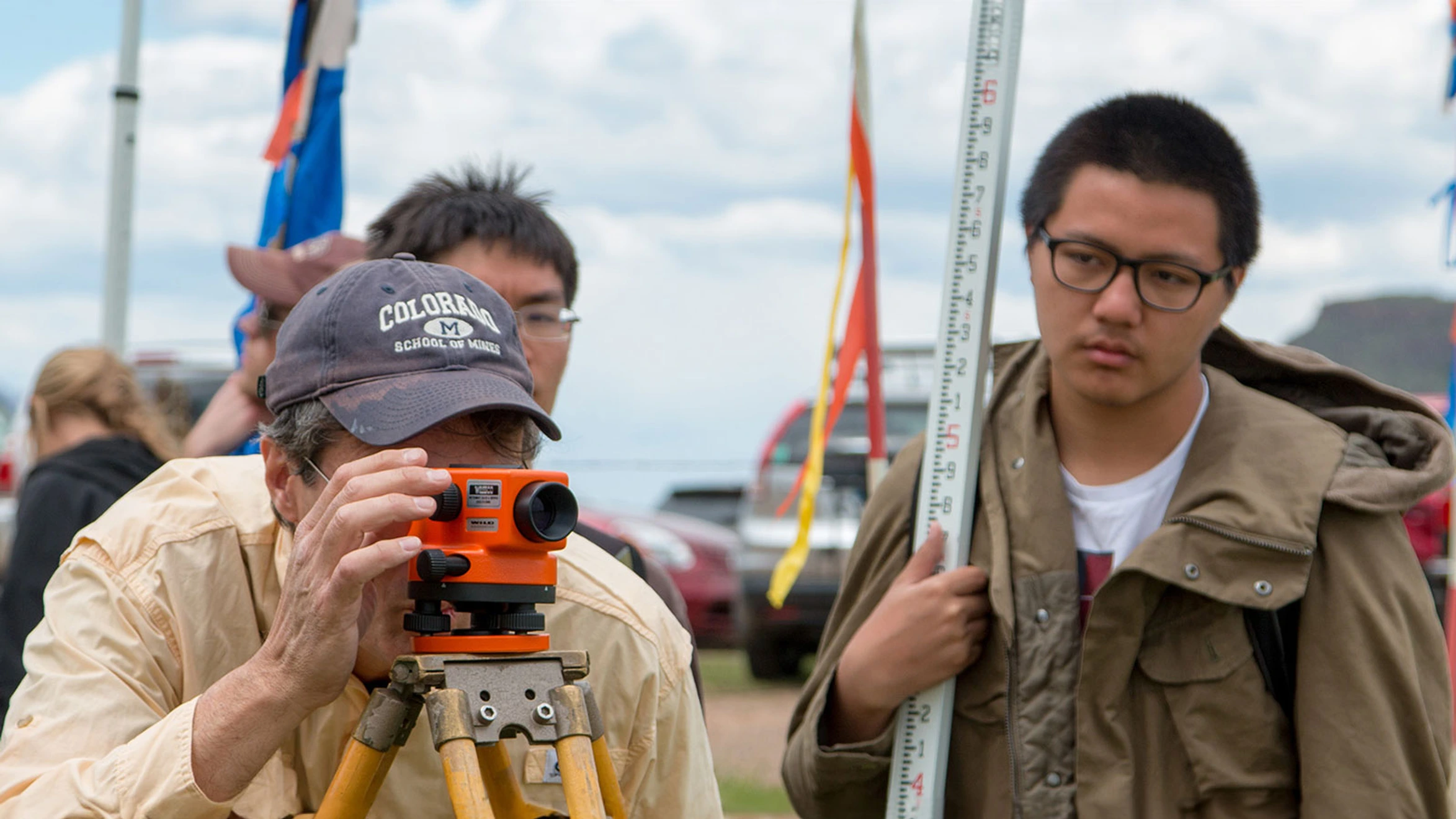 A man using a theodolite on a tripod in front of a group of people.