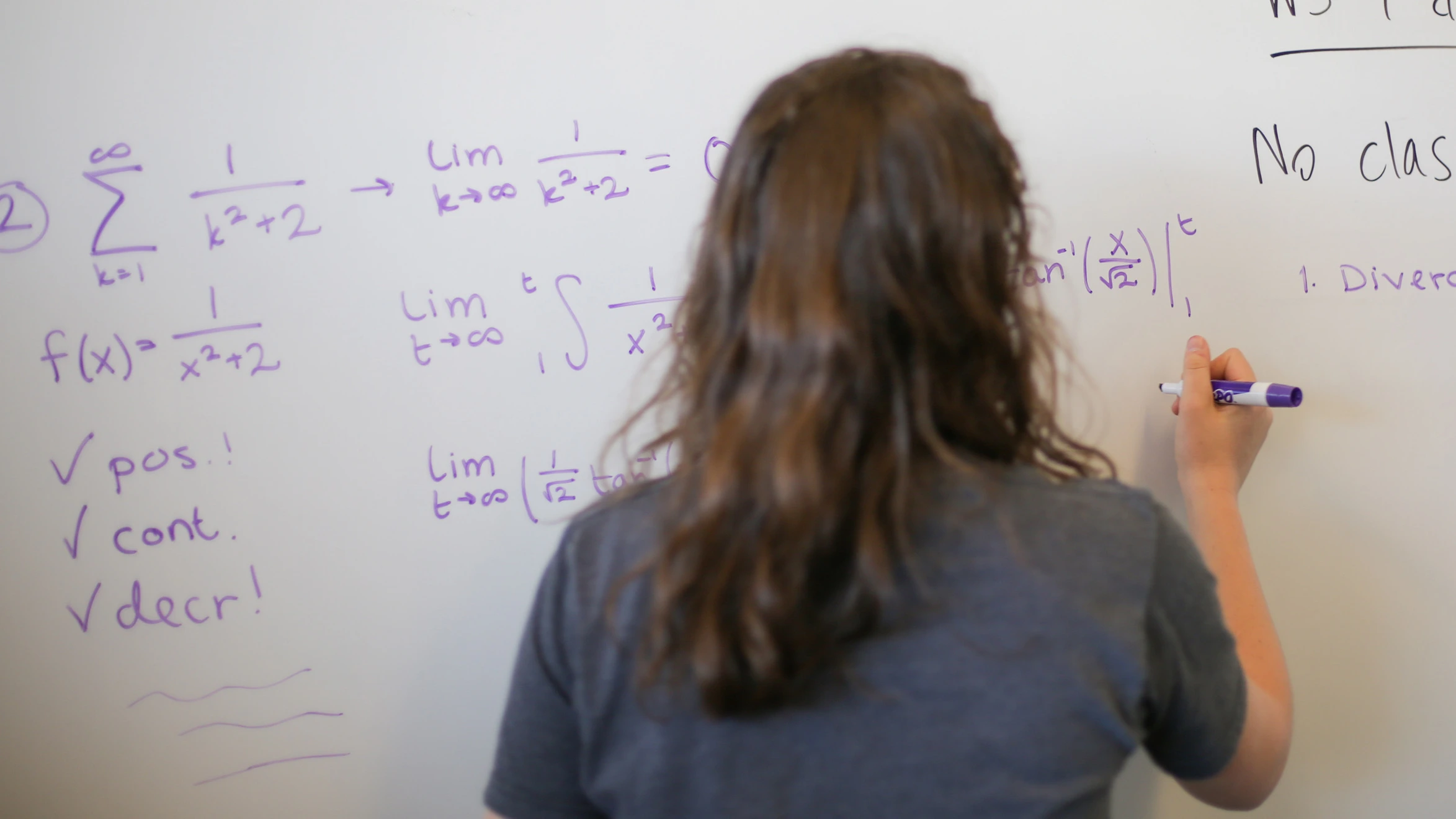 A woman writing on a whiteboard with a marker.