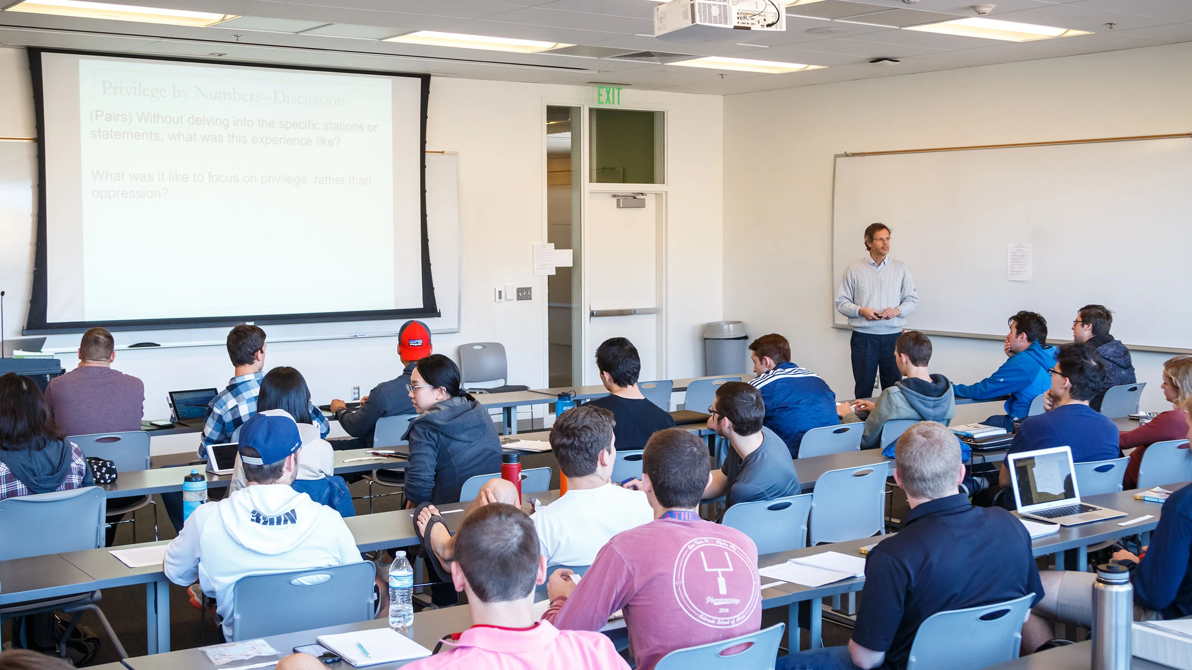 A man giving a presentation to a large group of people in a classroom.