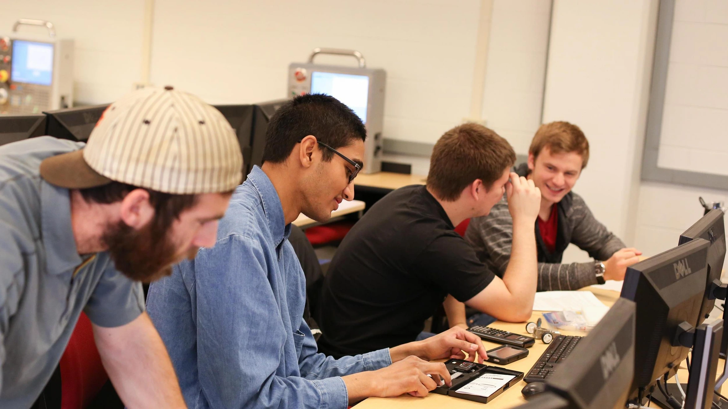 A group of men sitting around a computer in a classroom.