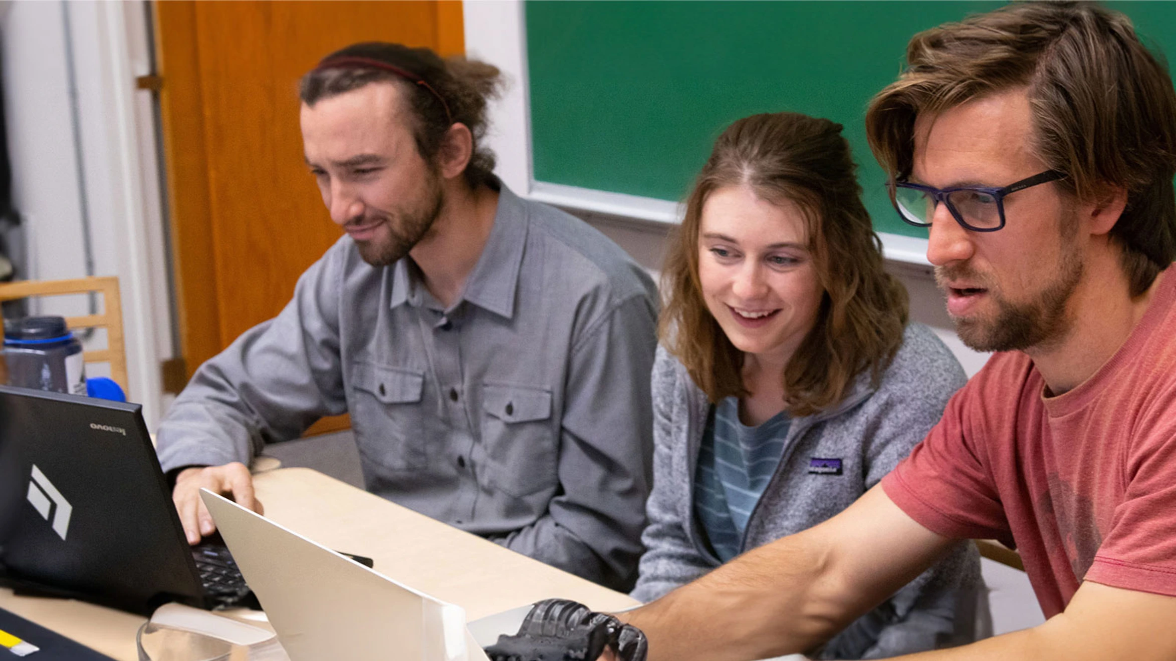 A group of people sitting around a table looking at a laptop.