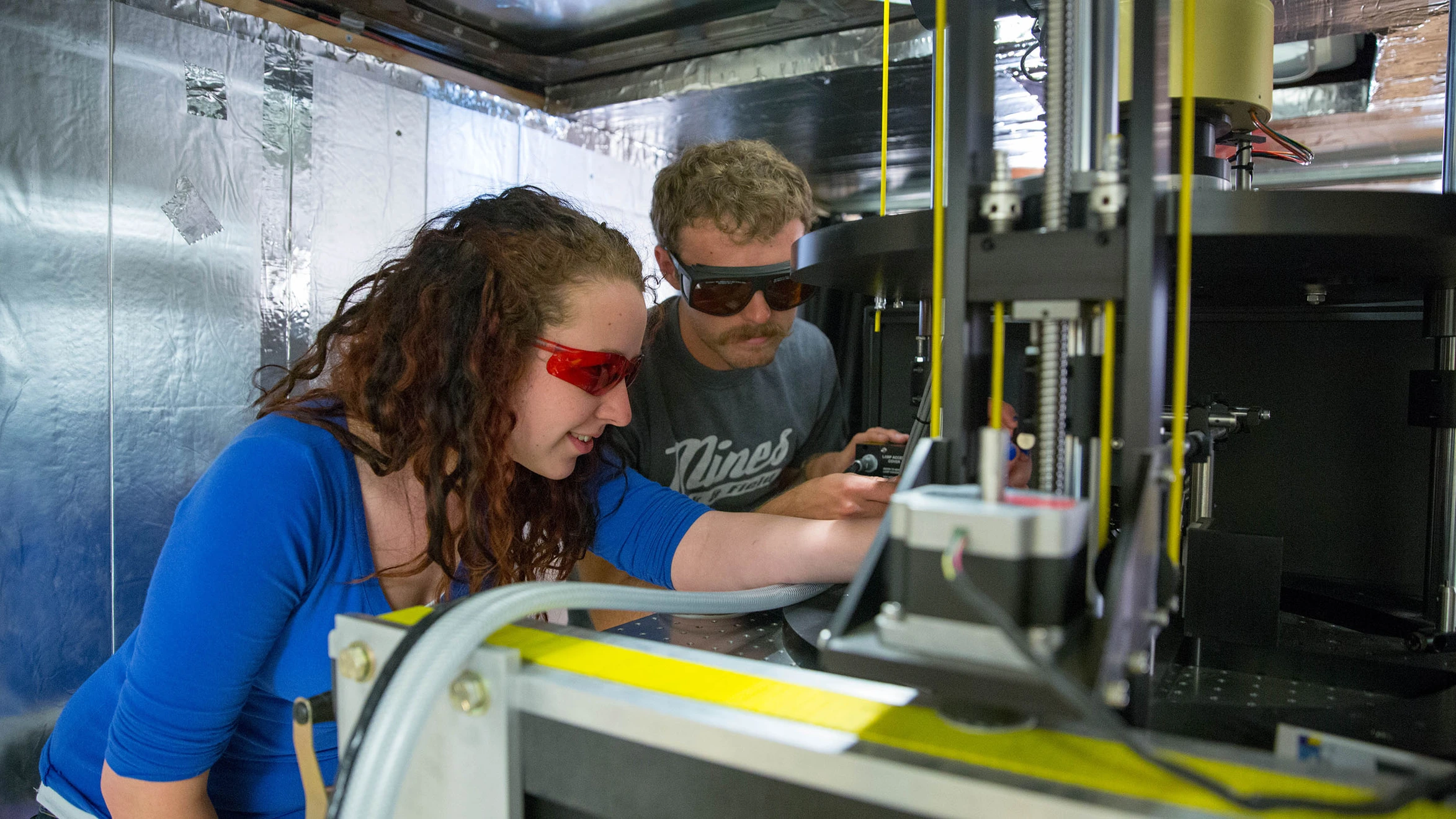 A man and a woman looking at a 3D printer.