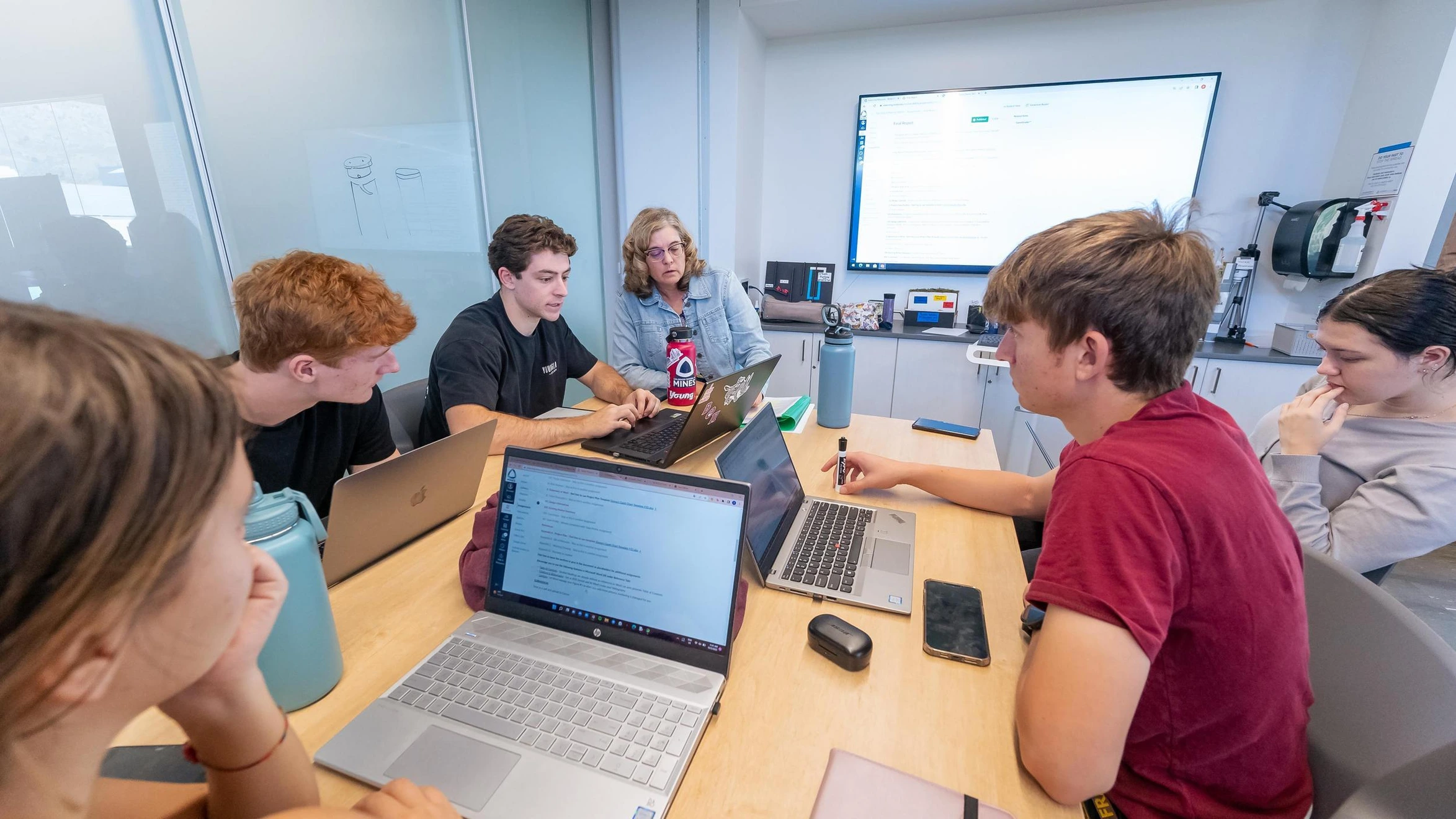 A group of people sitting around a table with laptops.