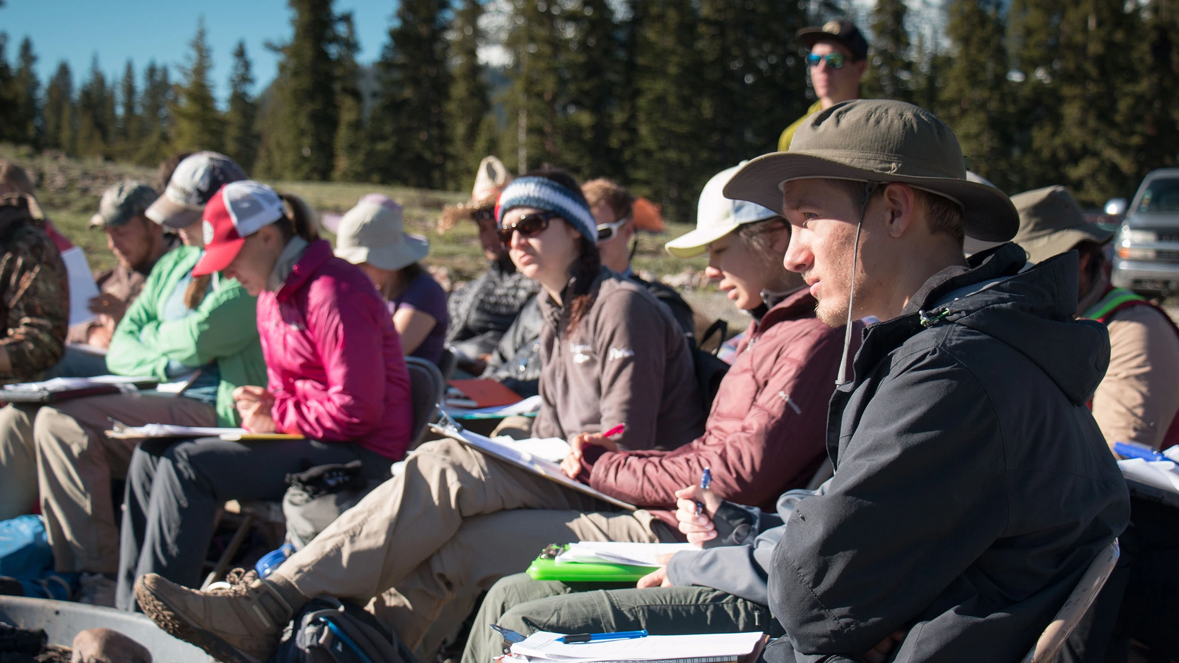 A group of people sitting in a field with hats on.