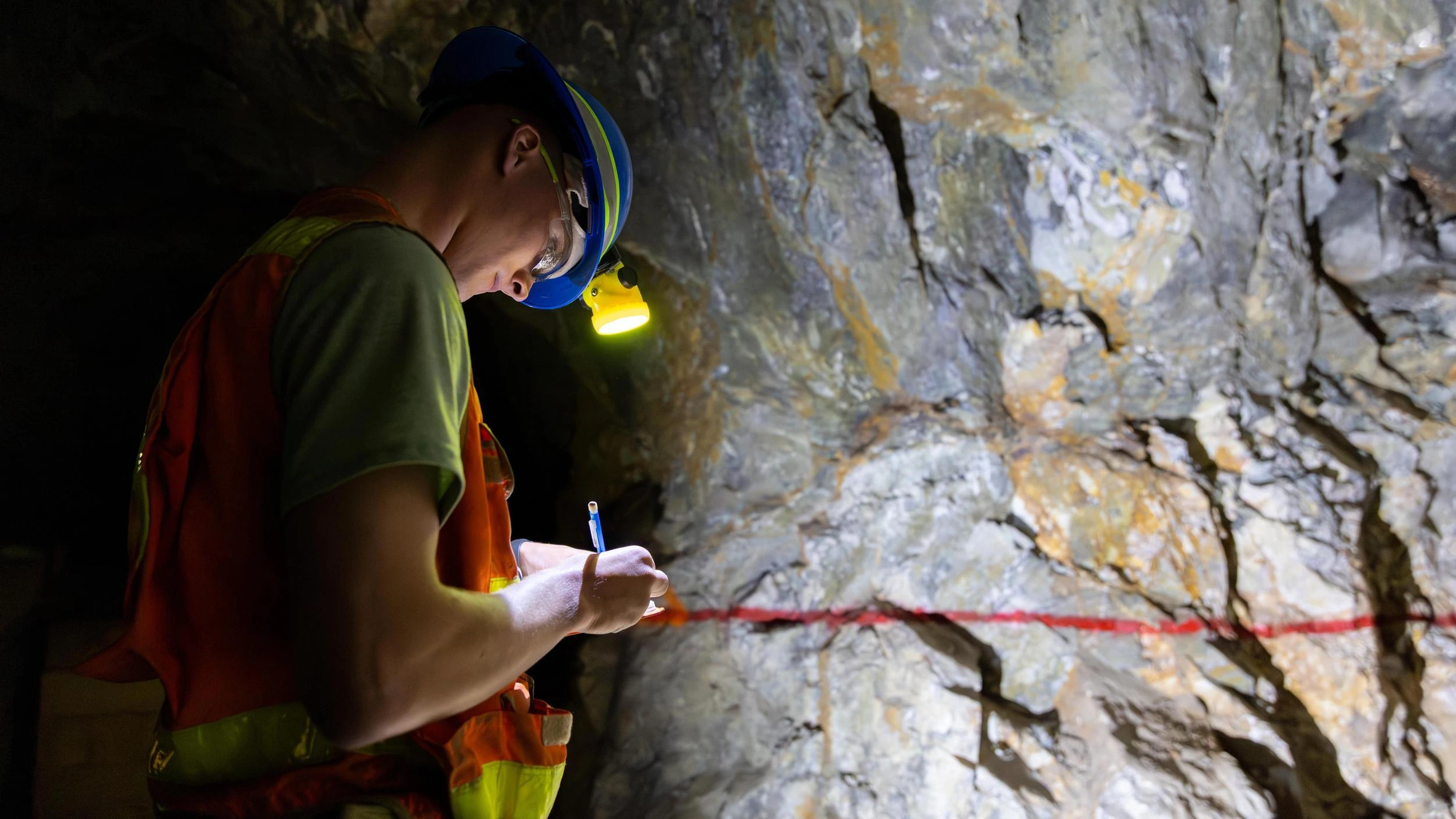 A man in a hard hat and safety vest writing on a piece of paper.