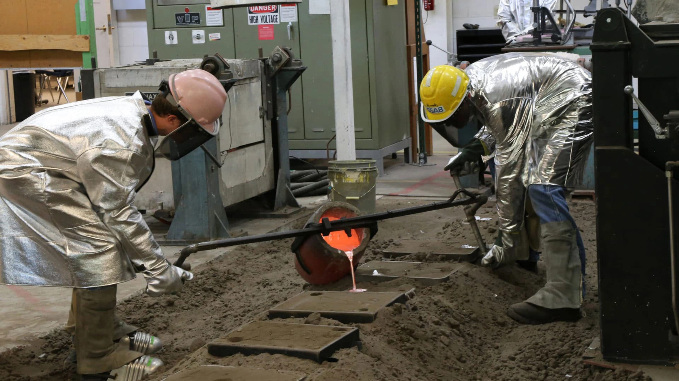 Two men in protective gear working in a factory.