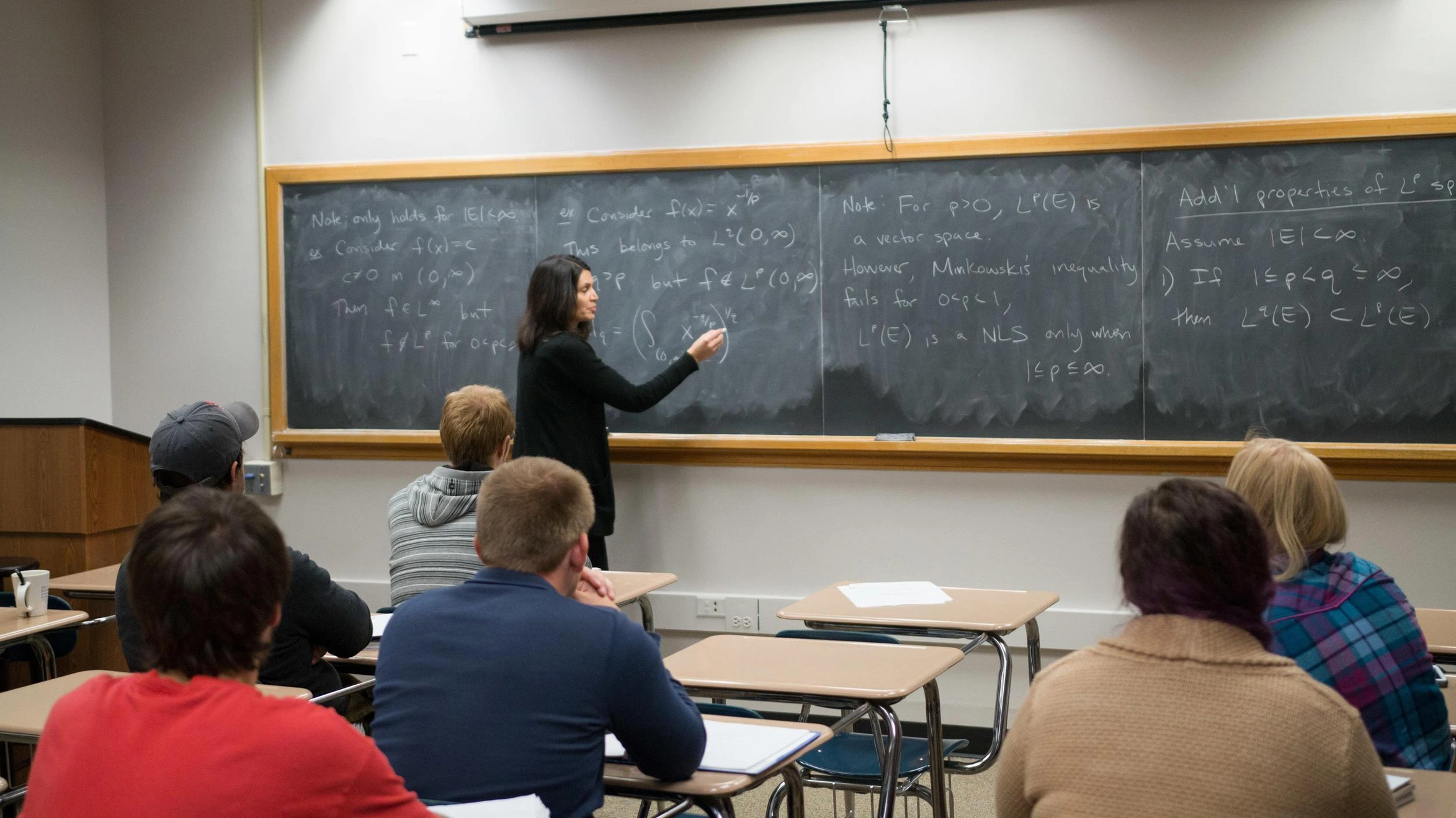A woman standing in front of a blackboard in a classroom.