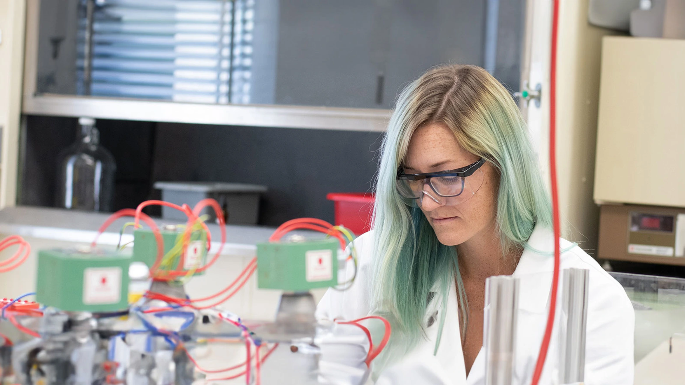 A woman in a lab coat and glasses working on a machine.