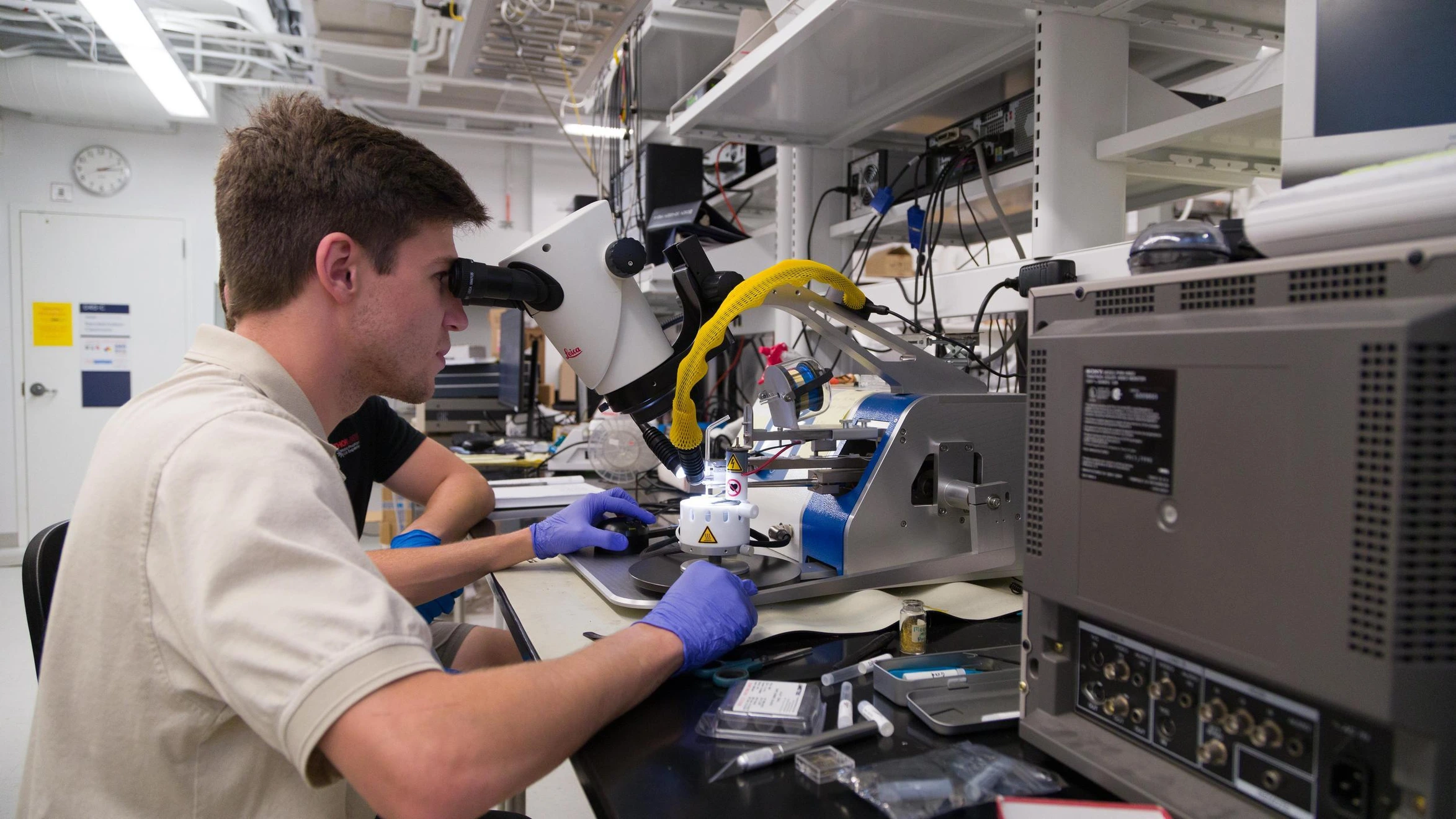 A man in a lab looking through a microscope.