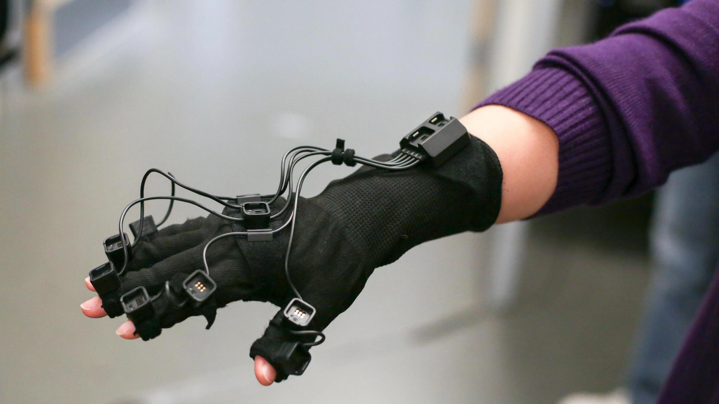 A person wearing a pair of black gloves with wires attached to them.