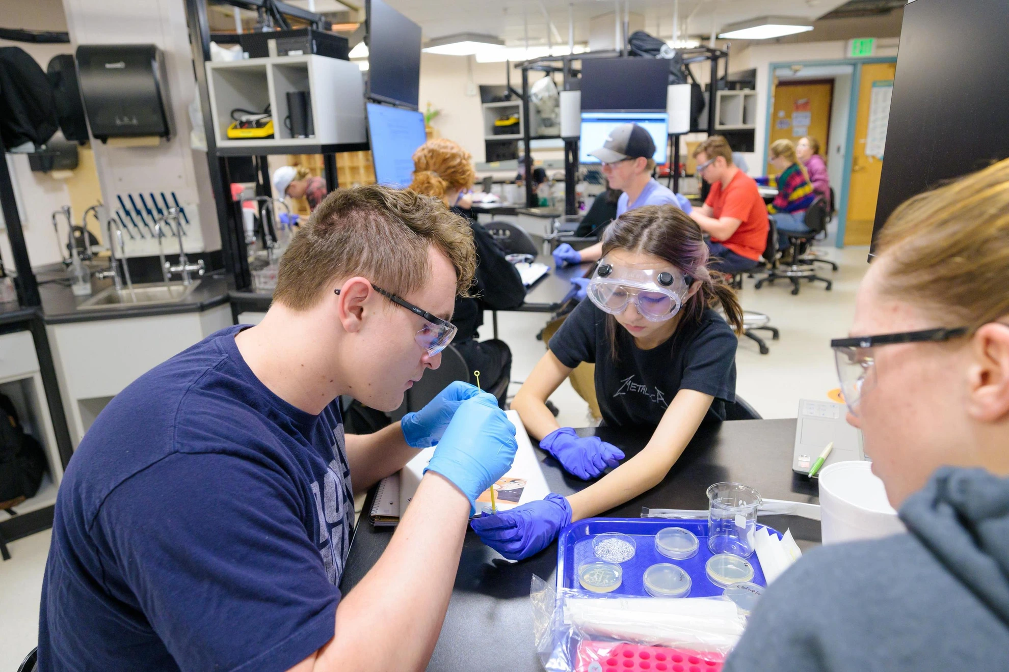 Students wearing protective eyewear and gloves conduct a hands-on science experiment in a laboratory.