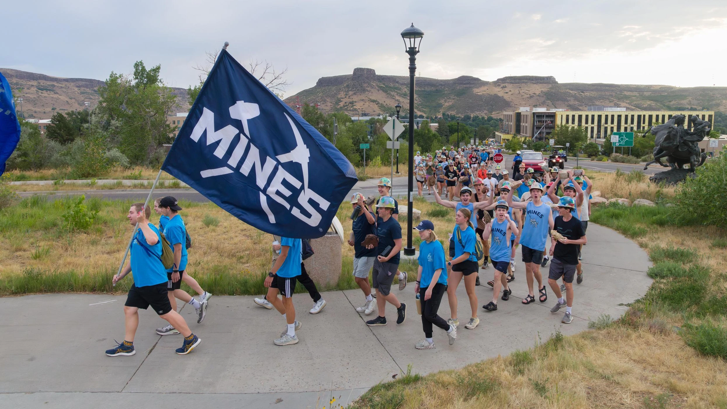 Group of Mines students marching outdoors with a large flag reading 