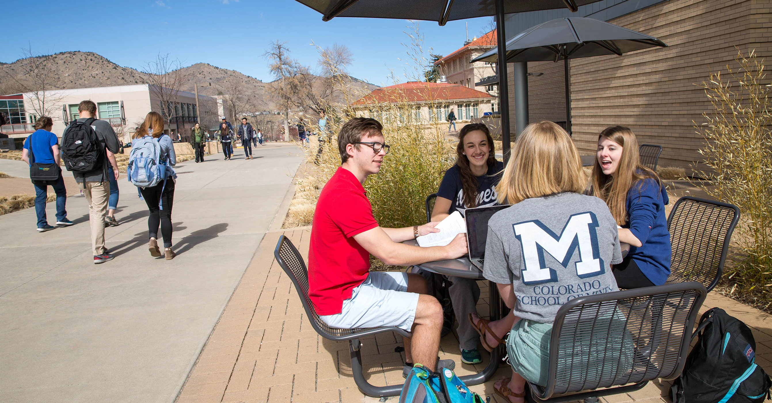 Mines students sitting at a table on Mines campus plaza with blue sky and mountains in the background