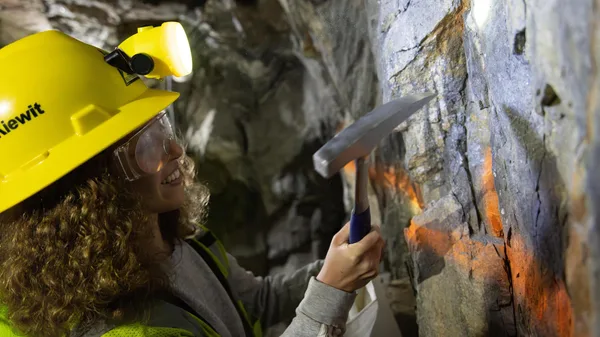 A Colorado School of Mines Geology student wears a hard hat and practices mineral identification with a pick axe in Edgar Mine.