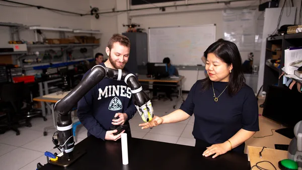 A man and a woman standing next to a table with a robot.