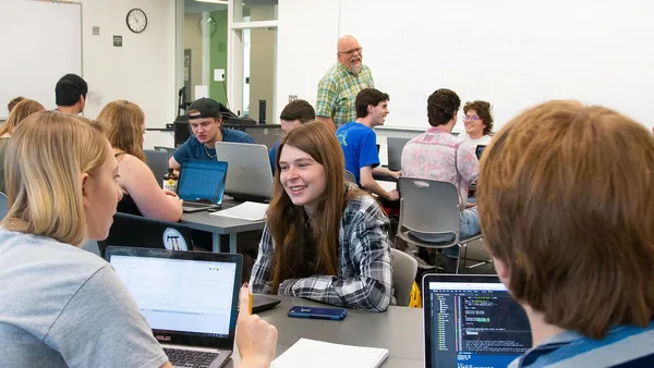 A group of people sitting around a table with laptops.