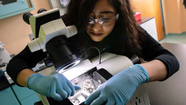 A woman in blue gloves looking through a microscope.