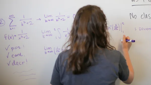 A woman writing on a whiteboard with a marker.