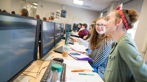 A group of young women sitting at a desk in front of computers.