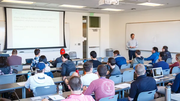A man giving a presentation to a large group of people in a classroom.