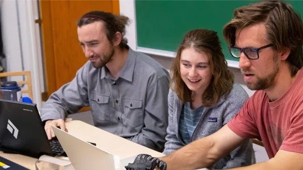 A group of people sitting around a table looking at a laptop.