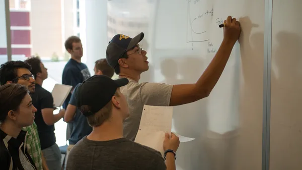 A group of people standing around a whiteboard writing on it.