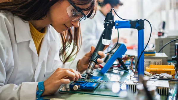 A woman in a lab coat working on a circuit board.