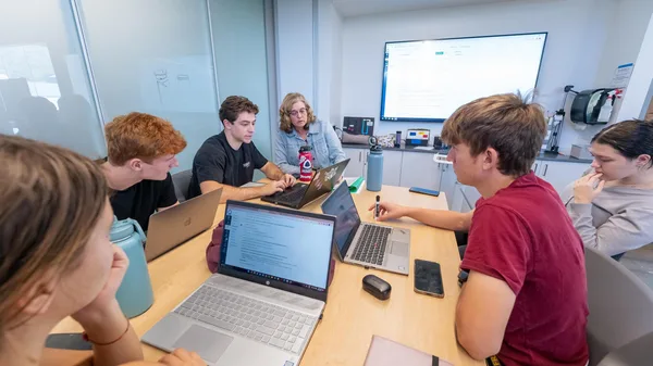 A group of people sitting around a table with laptops.