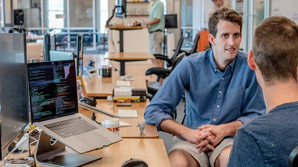 two men sitting at a desk in front of a computer.