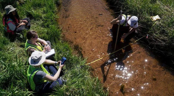 A group of people sitting on the ground next to a stream.