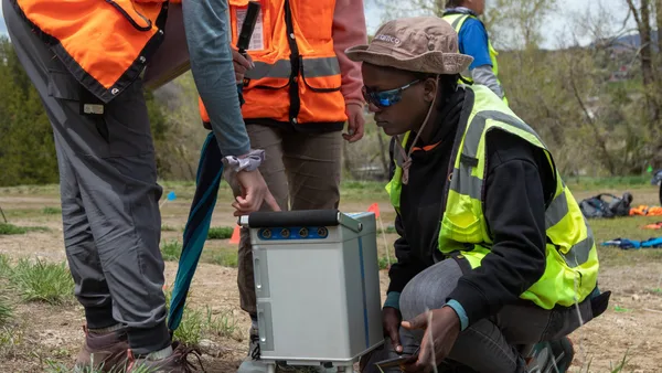 A group of people in safety vests and hard hats looking at a device.