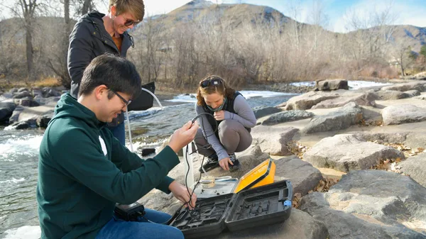 A group of people sitting on top of a rock next to a river.
