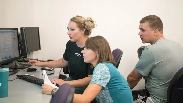 A group of people sitting around a desk in front of a computer.