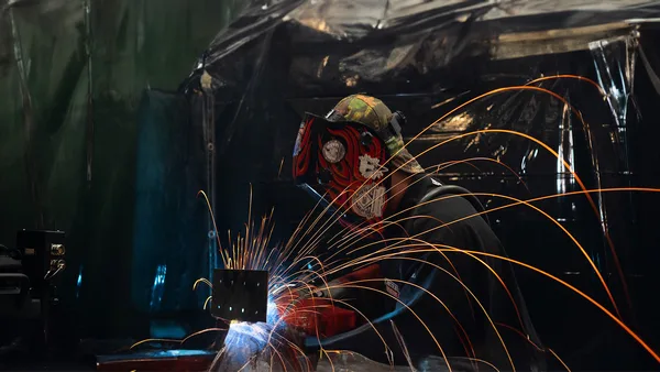 A welder working on a piece of metal with sparks.