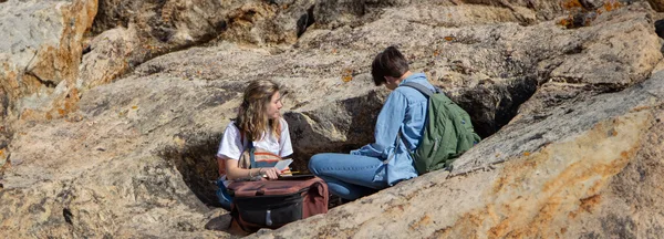 A couple of people sitting on top of a large rock.