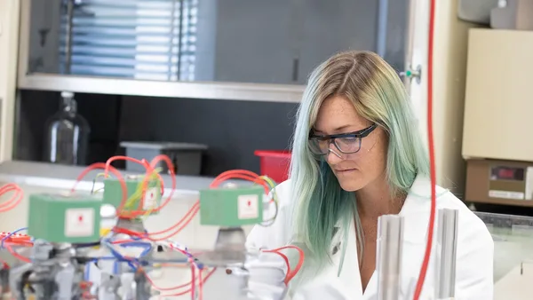 A woman in a lab coat and glasses working on a machine.