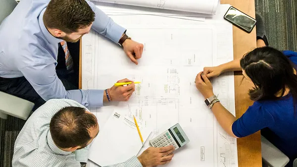 A group of people sitting around a table looking at blueprints.