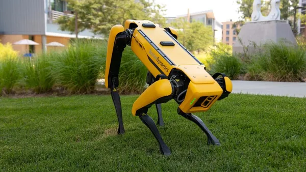 a yellow and black robot sitting on top of a lush green field.