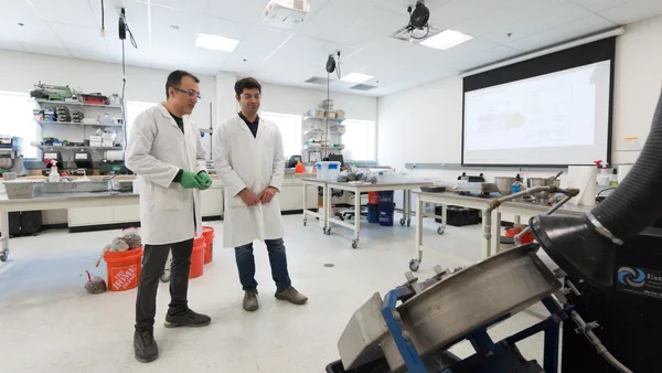 Two men in lab coats standing next to each other in a lab.