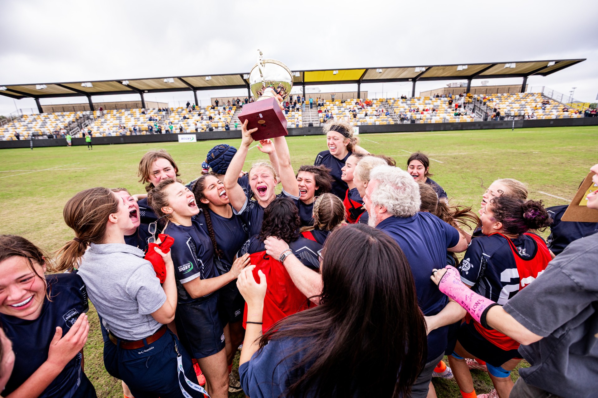Mines Womens Club Rugby Team celebrates with one player in center holding trophy over her head