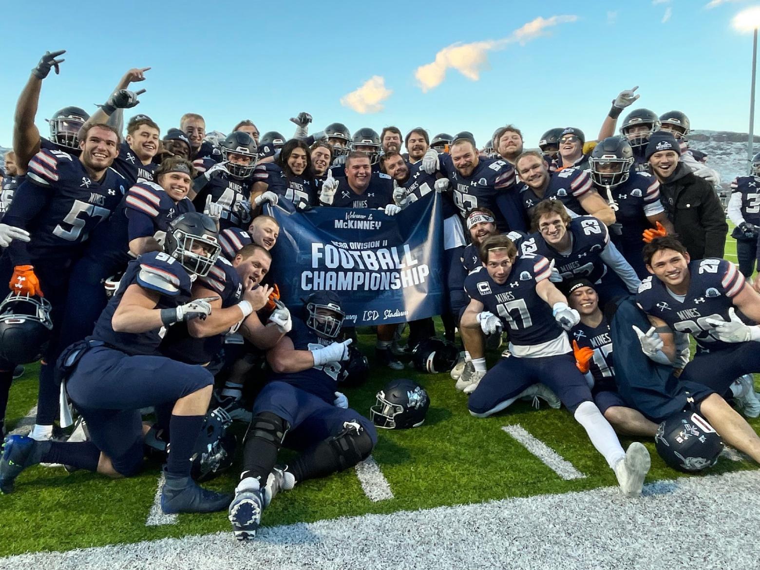 Mines Orediggers Football team poses on the field holding up an NCAA Division 2 Football Championship banner.