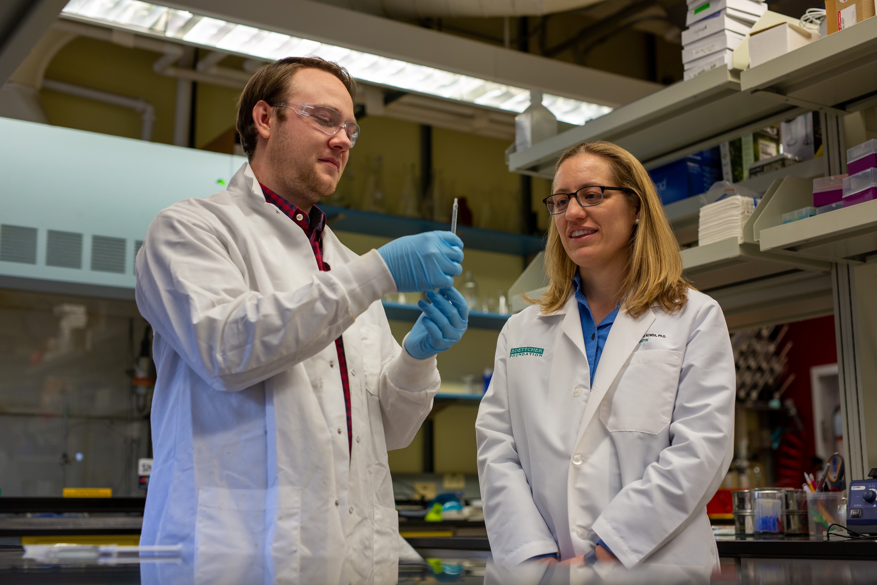 Melissa Krebs and a male graduate student inspect an instrument in a lab on campus